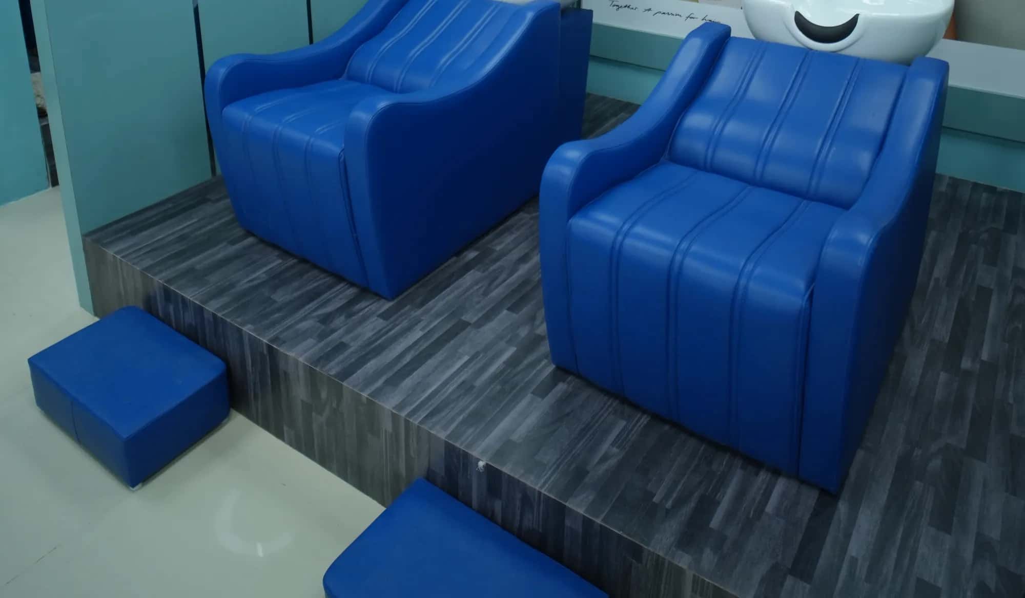 Two royal blue shampoo chairs with white wash basins on a raised grey floor at the hair wash station
