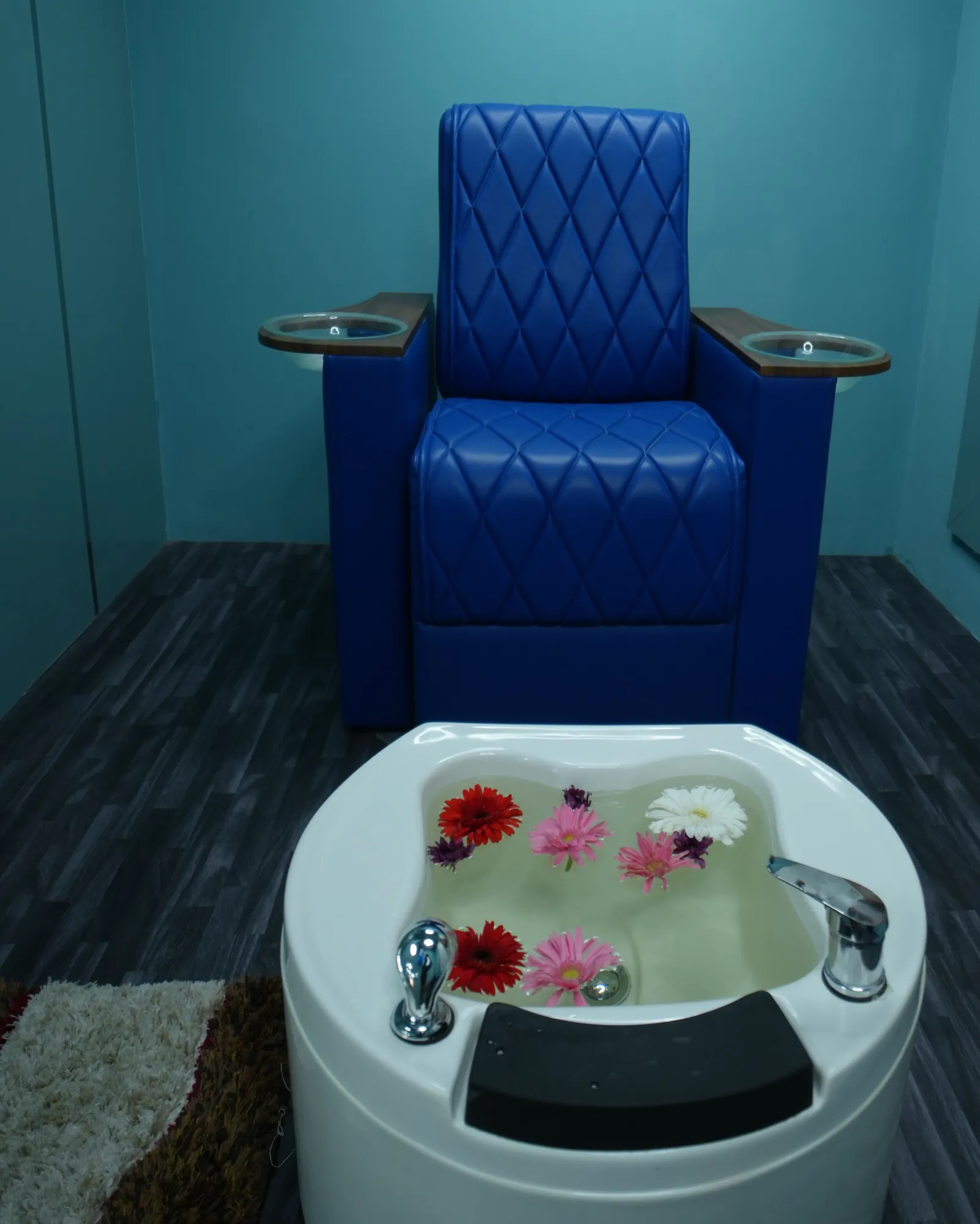 Royal blue quilted pedicure chair with a white basin of floating flowers in a teal room