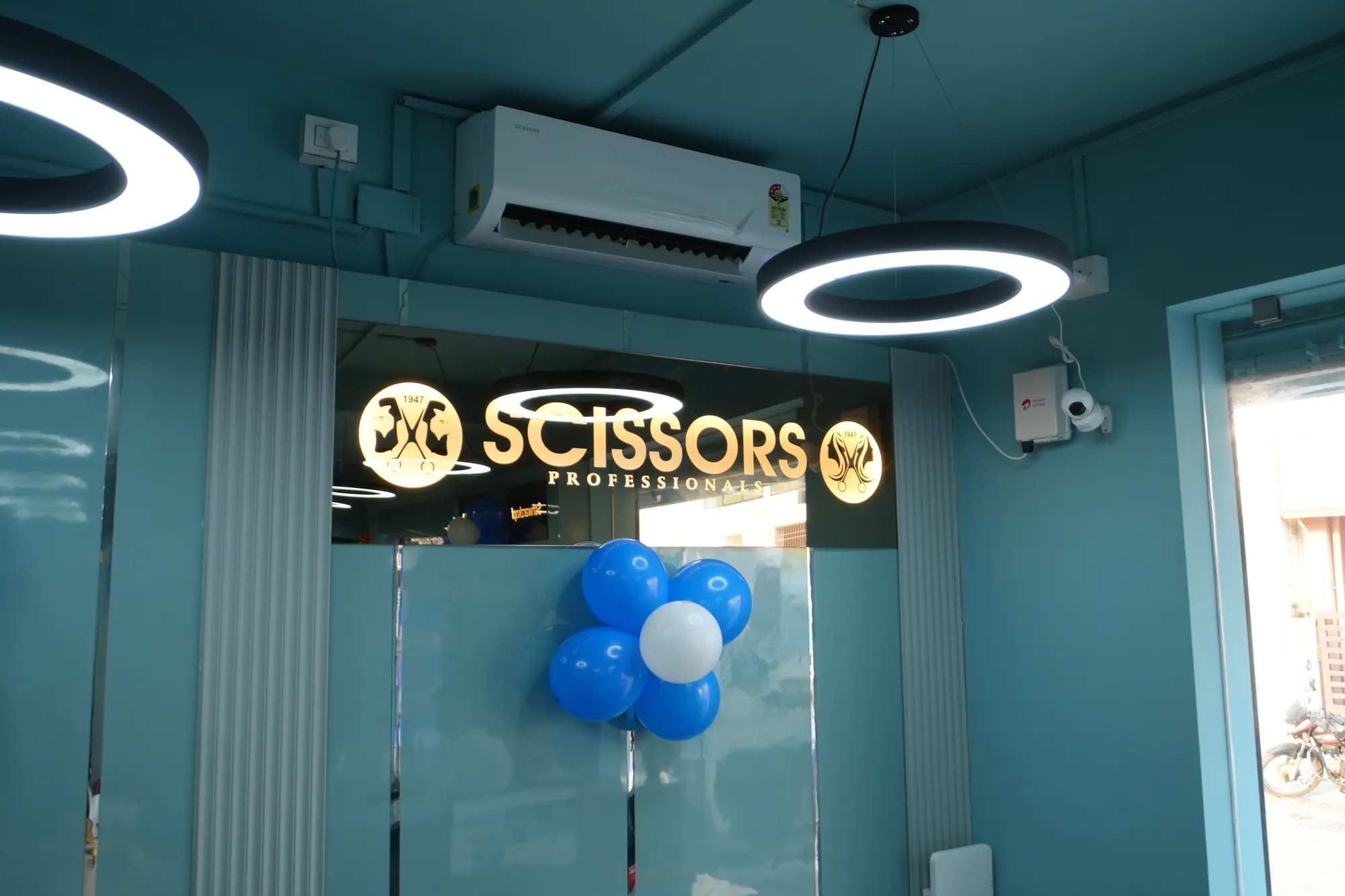 Illuminated gold Scissors Professionals sign above the reception with a blue and white balloon cluster and ring pendant lights, Kolapakkam