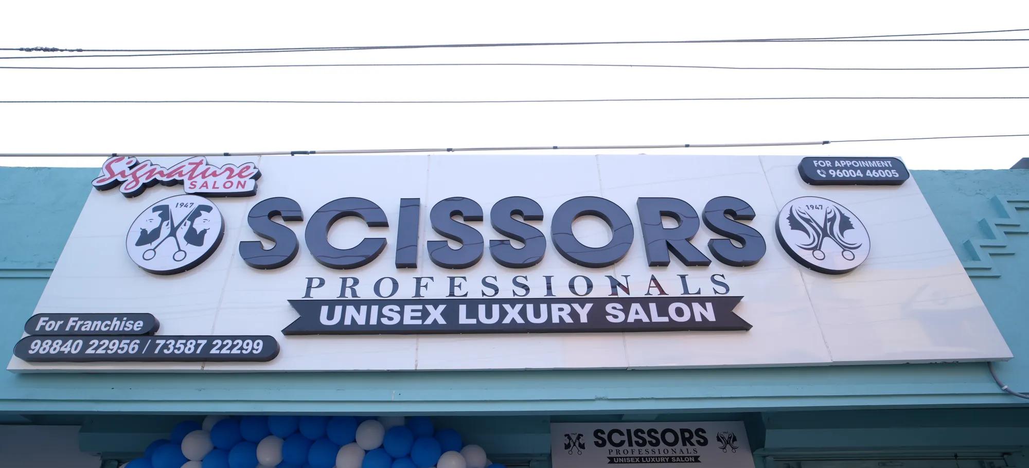 Scissors Professionals Unisex Luxury Salon signboard above a blue and white balloon arch at the Kolapakkam entrance