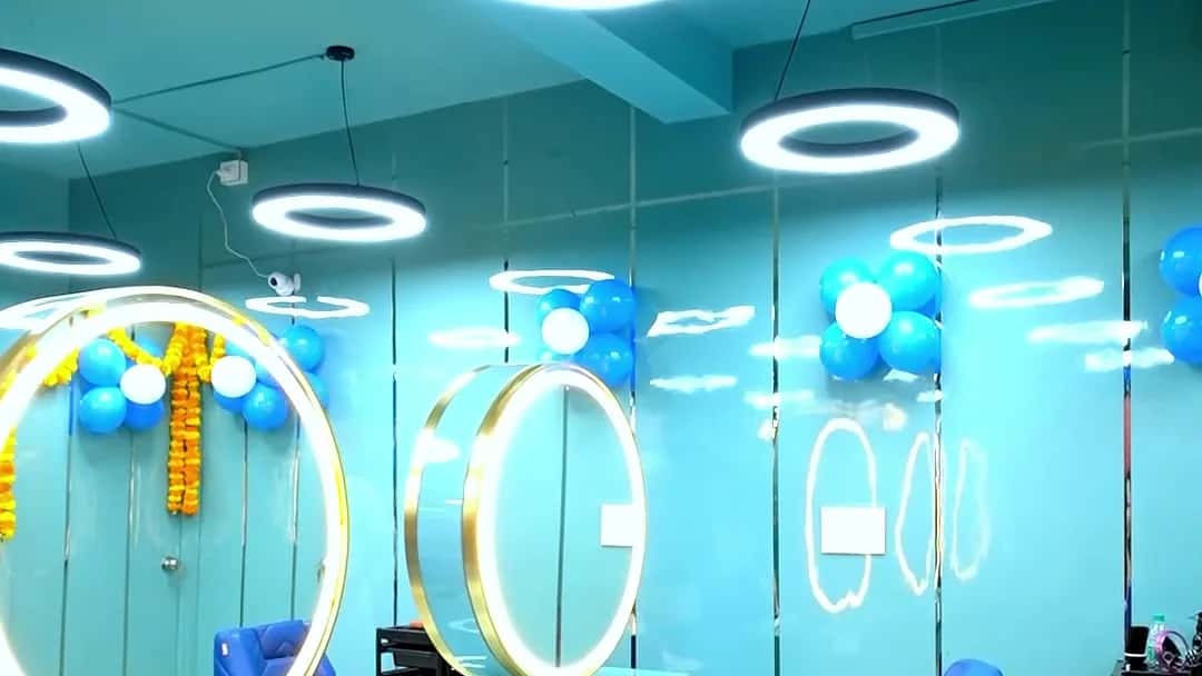 Row of gold ring mirrors above a teal styling counter with royal blue chairs and ring pendant lights