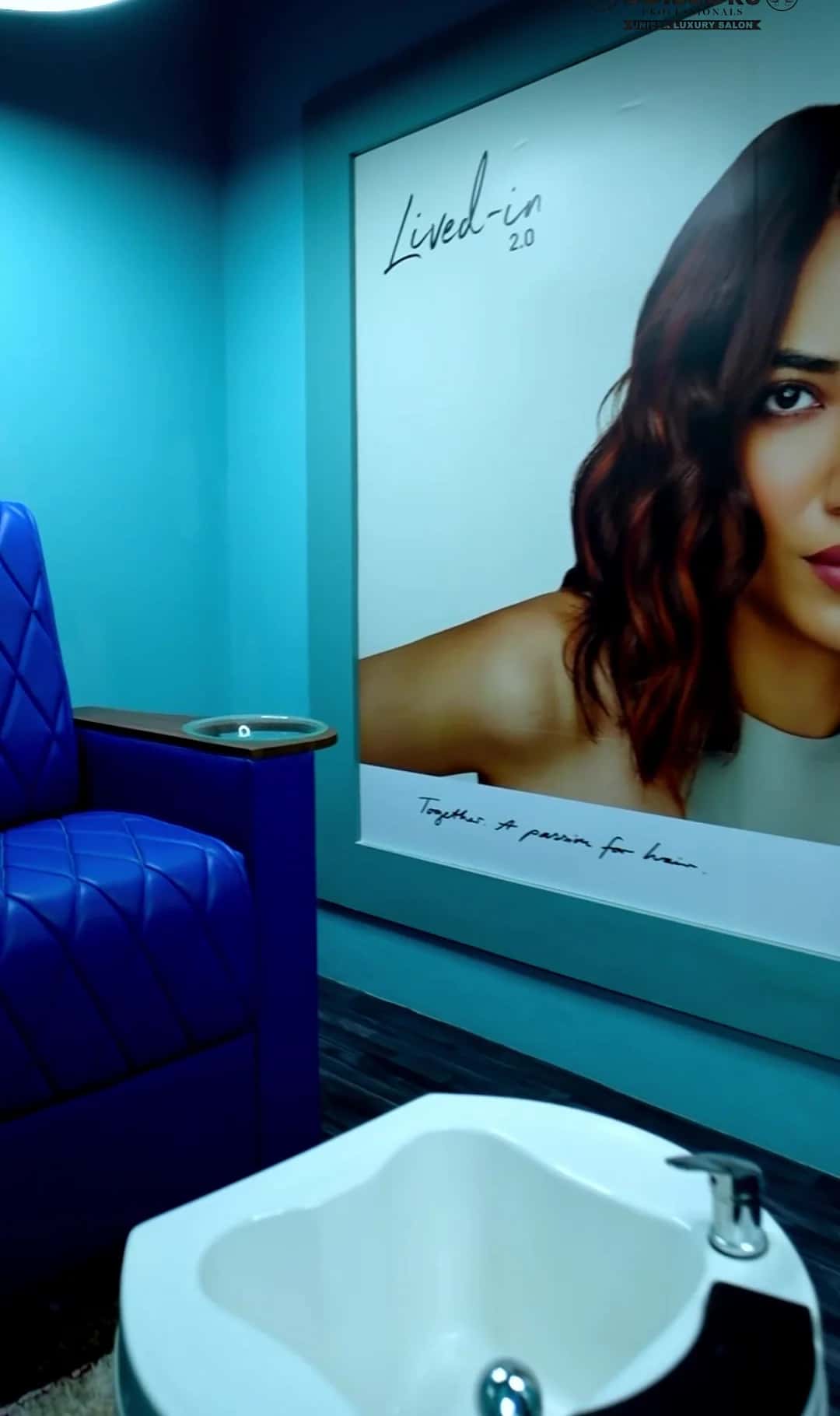 Royal blue quilted chair with a white pedicure basin beside a wall poster of wavy hair