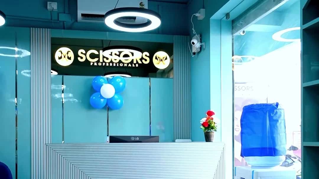 Reception desk with the illuminated Scissors Professionals sign, blue balloon cluster and water dispenser at Scissors Professionals Kolapakkam