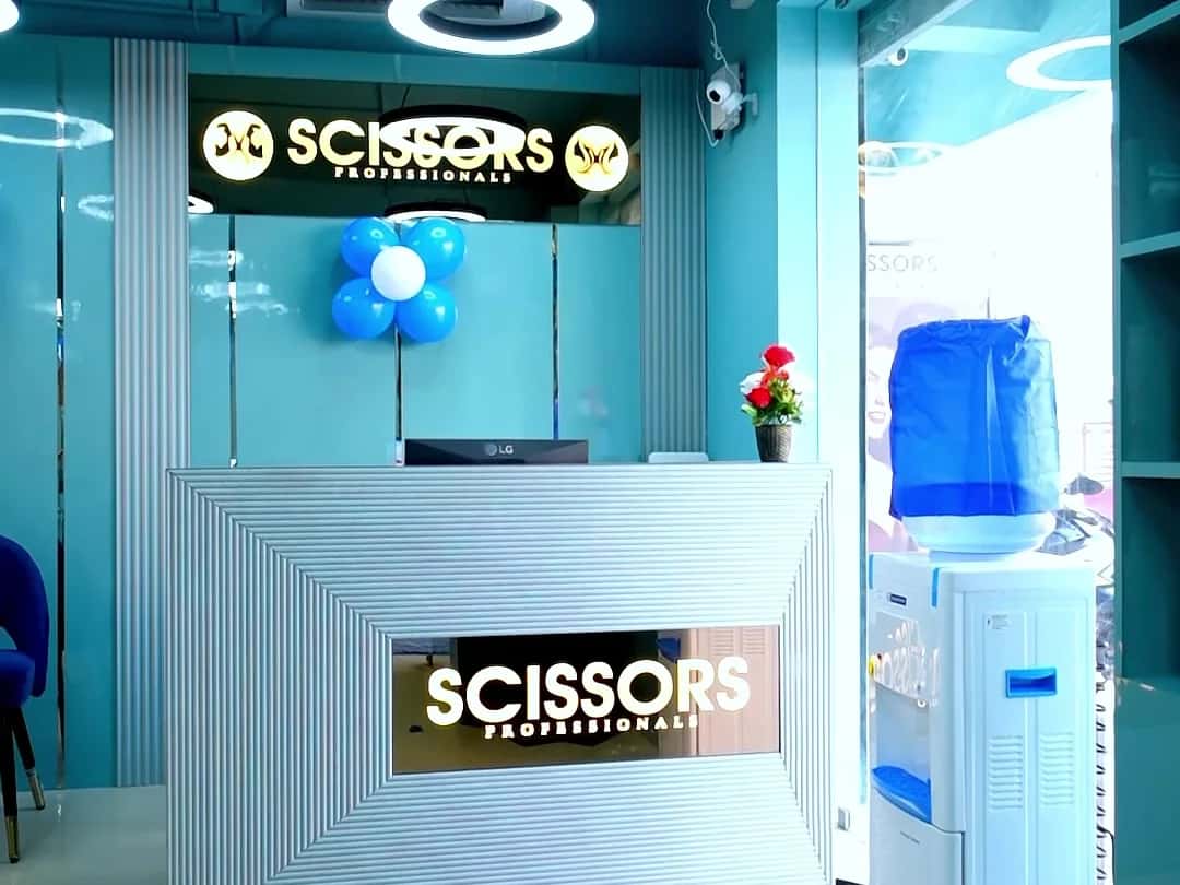 Reception desk with the illuminated Scissors Professionals sign, blue balloon cluster and water dispenser at Scissors Professionals Kolapakkam