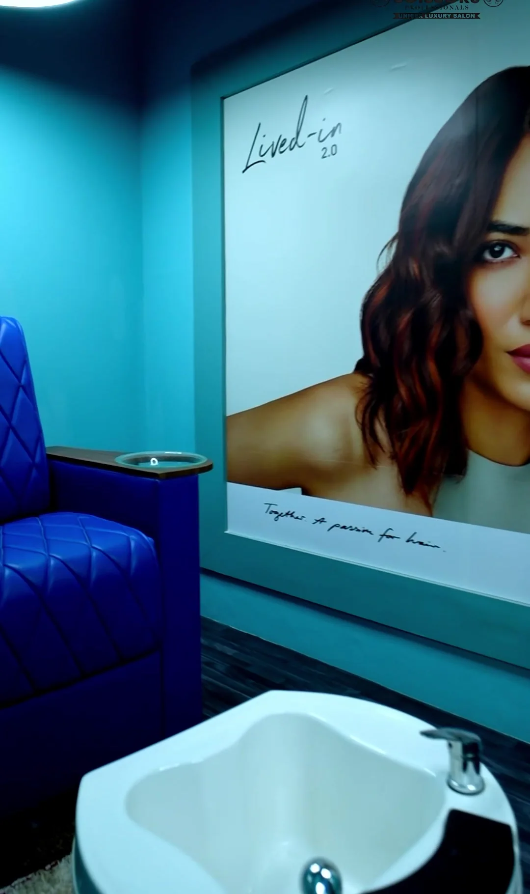 Royal blue quilted chair with a white pedicure basin beside a wall poster of wavy hair