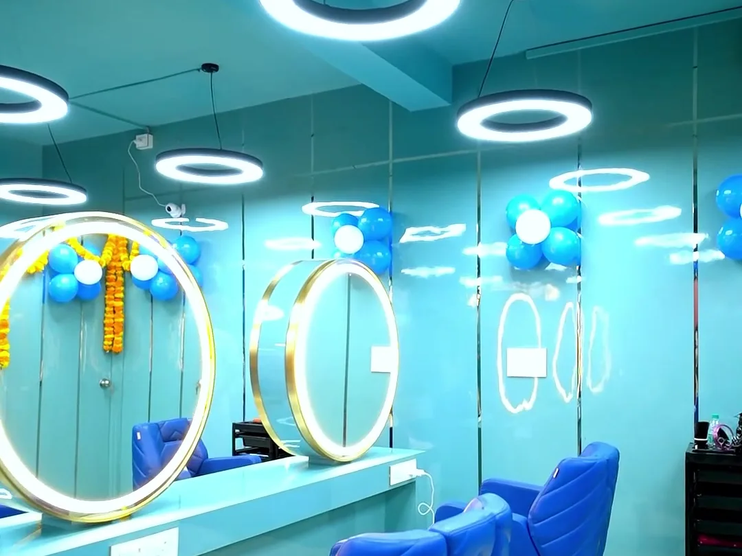 Row of gold ring mirrors above a teal styling counter with royal blue chairs and ring pendant lights