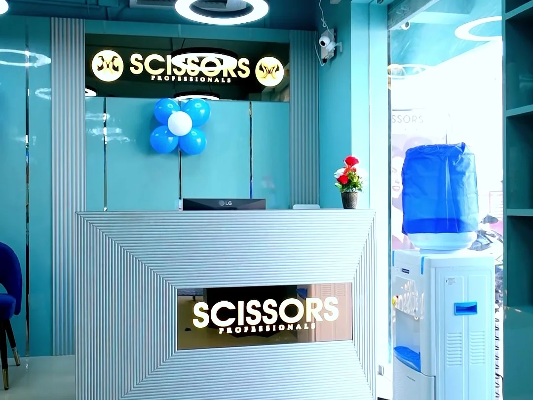 Reception desk with the illuminated Scissors Professionals sign and blue balloon cluster at the Kolapakkam salon